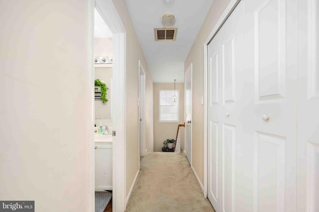 hall featuring visible vents, a sink, and light colored carpet