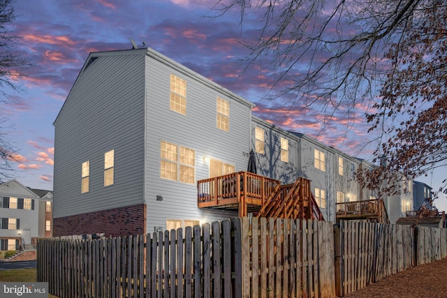 back of house at dusk with fence private yard, a deck, and brick siding