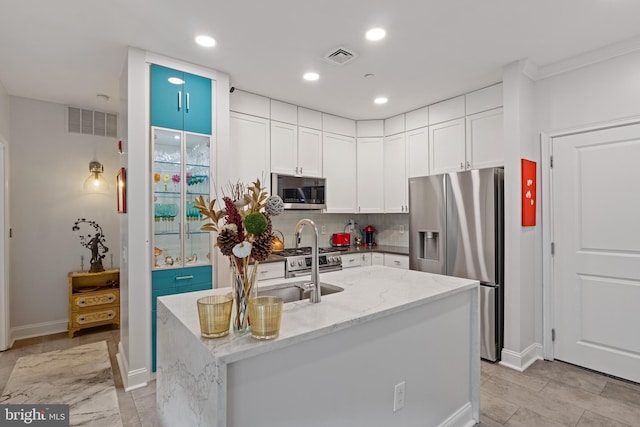 kitchen with light stone counters, a center island with sink, stainless steel appliances, visible vents, and white cabinetry