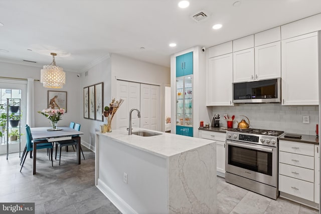 kitchen with stainless steel appliances, a sink, white cabinetry, decorative backsplash, and an island with sink