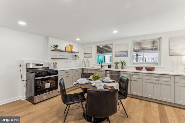 kitchen featuring appliances with stainless steel finishes, light countertops, light wood-type flooring, open shelves, and a sink