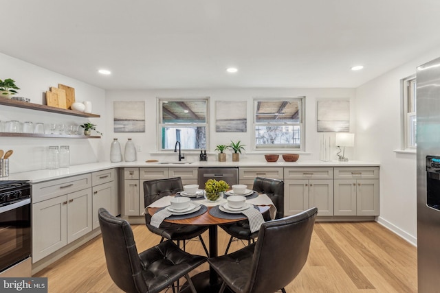 kitchen with open shelves, light countertops, appliances with stainless steel finishes, light wood-style floors, and a sink