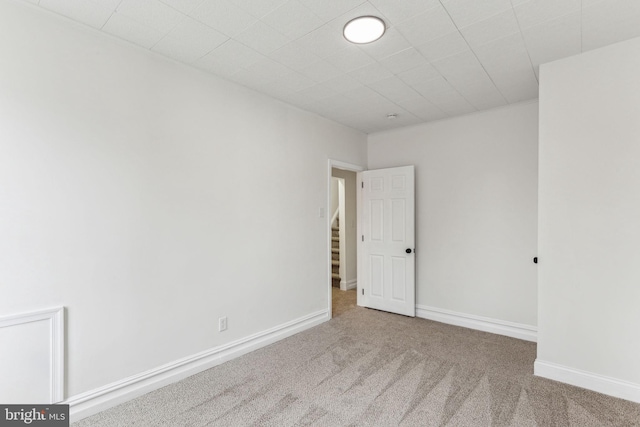 empty room featuring carpet floors, stairway, and baseboards