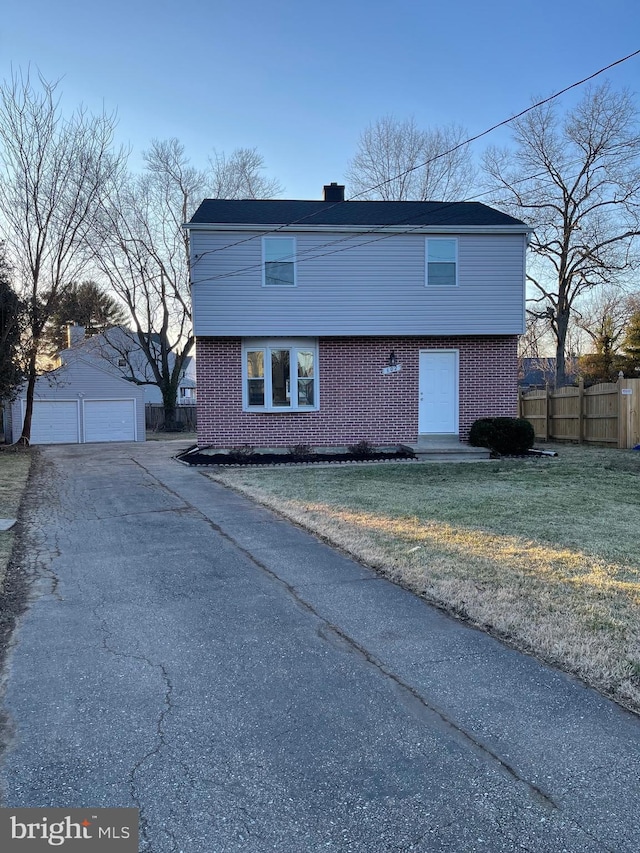 colonial home with brick siding, an outdoor structure, fence, a detached garage, and a front lawn