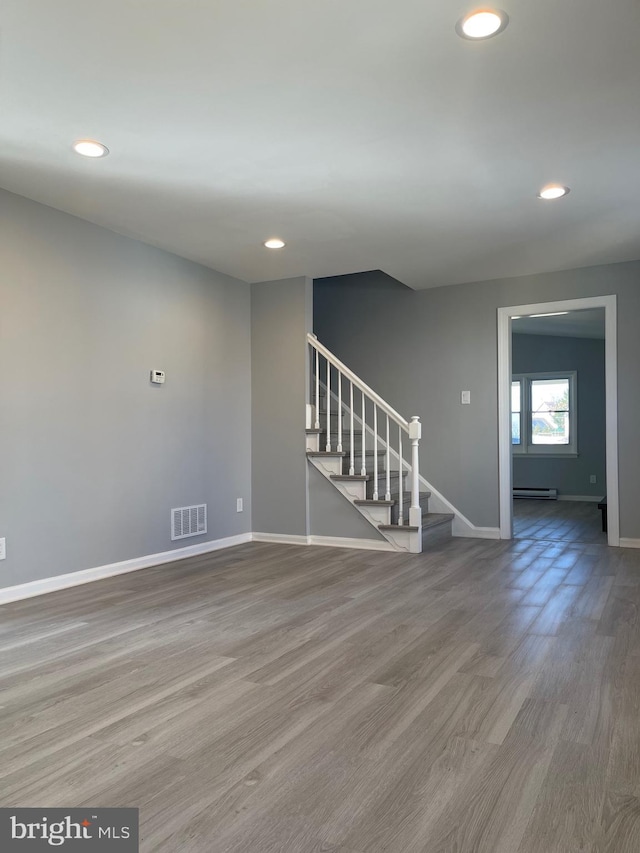 interior space featuring visible vents, stairway, baseboard heating, wood finished floors, and baseboards