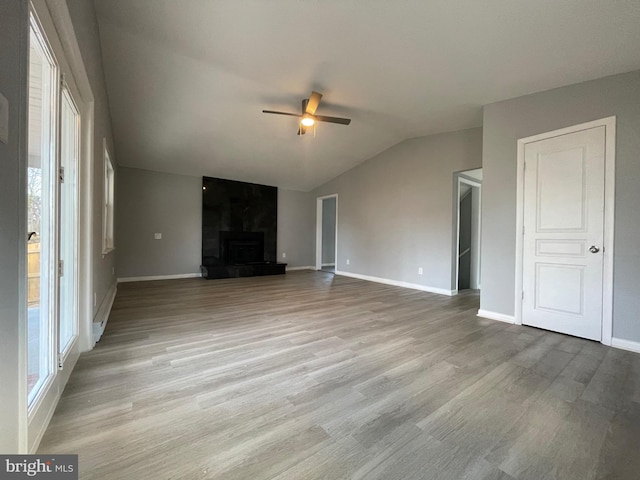 unfurnished living room with light wood-style flooring, a ceiling fan, a large fireplace, vaulted ceiling, and baseboards