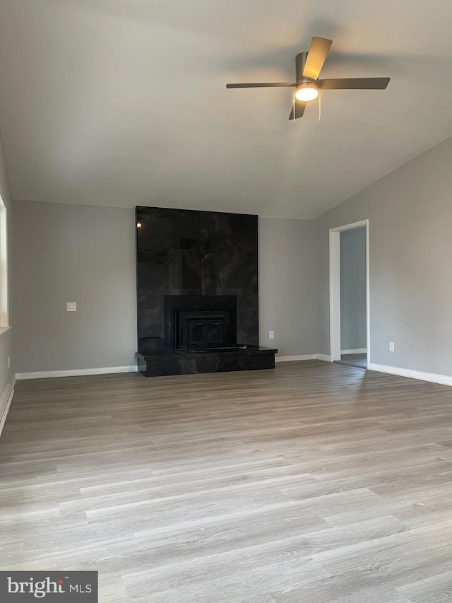 unfurnished living room with a large fireplace, a ceiling fan, baseboards, vaulted ceiling, and light wood-style floors