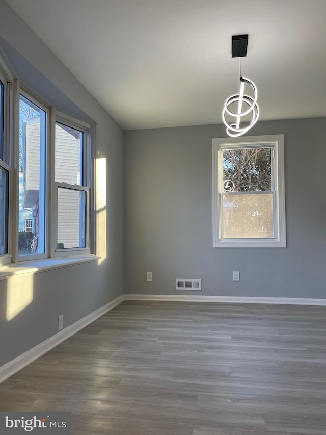 unfurnished dining area featuring an inviting chandelier, wood finished floors, visible vents, and baseboards