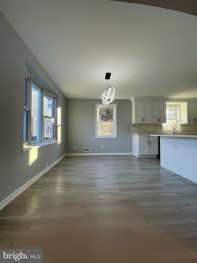 unfurnished living room with baseboards, visible vents, a sink, and wood finished floors