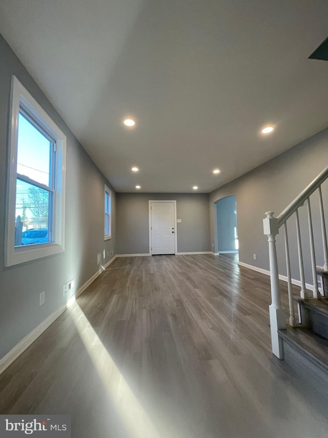 unfurnished living room with baseboards, stairs, arched walkways, and wood finished floors