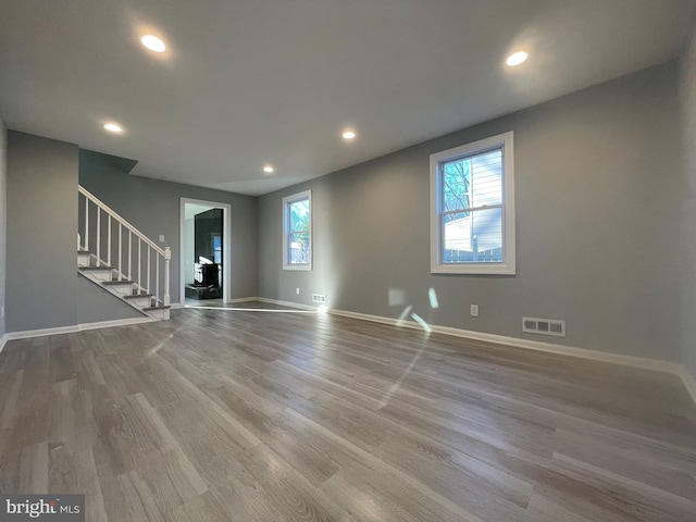 unfurnished living room featuring recessed lighting, visible vents, light wood-type flooring, baseboards, and stairs