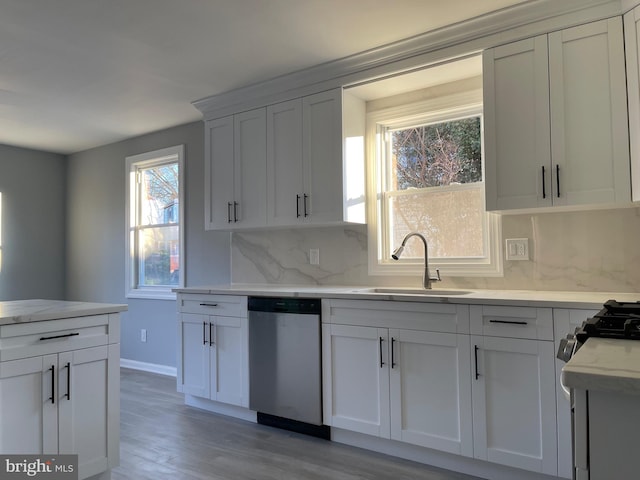 kitchen with light wood finished floors, backsplash, stainless steel dishwasher, white cabinetry, and a sink