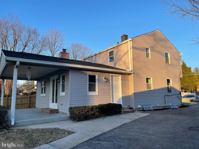 view of property exterior with entry steps, a patio, fence, a carport, and a chimney