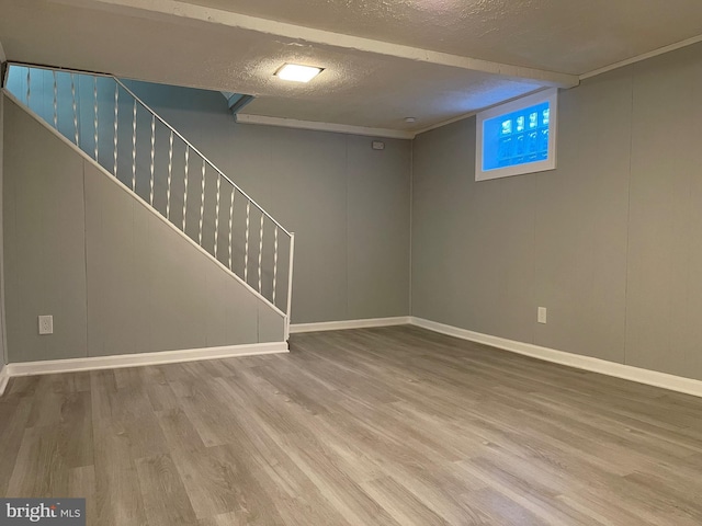 finished basement featuring light wood-style floors, a textured ceiling, baseboards, and stairs