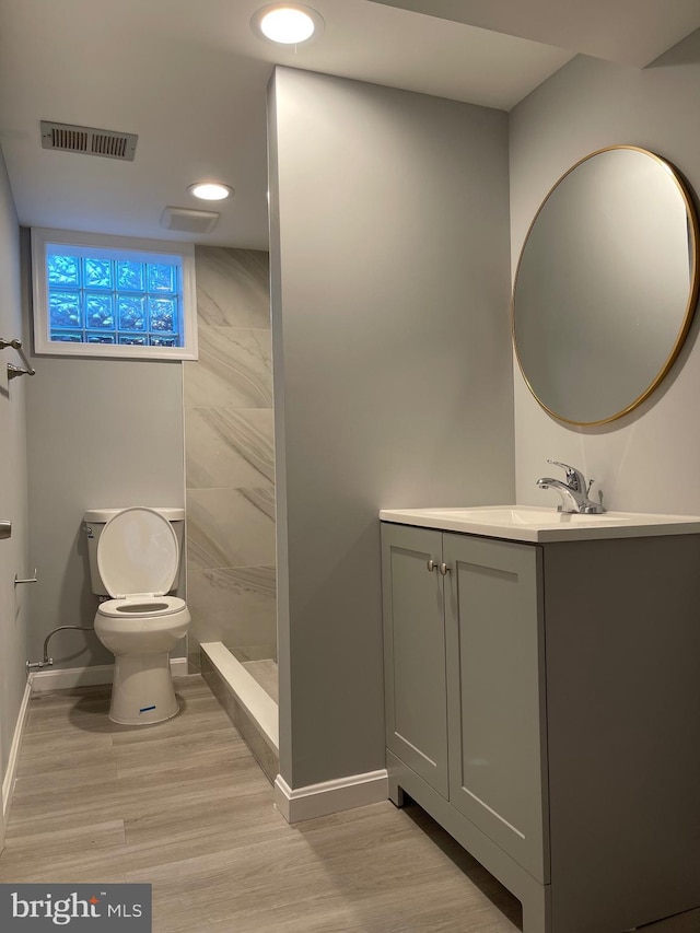 bathroom featuring visible vents, toilet, vanity, wood finished floors, and baseboards