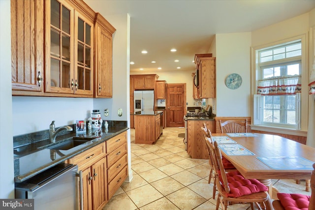 kitchen featuring a sink, dark countertops, stainless steel fridge, and glass insert cabinets