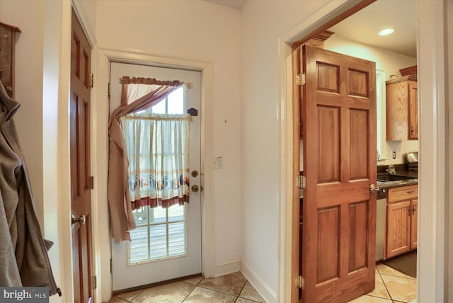 doorway to outside featuring light tile patterned floors, baseboards, and a sink