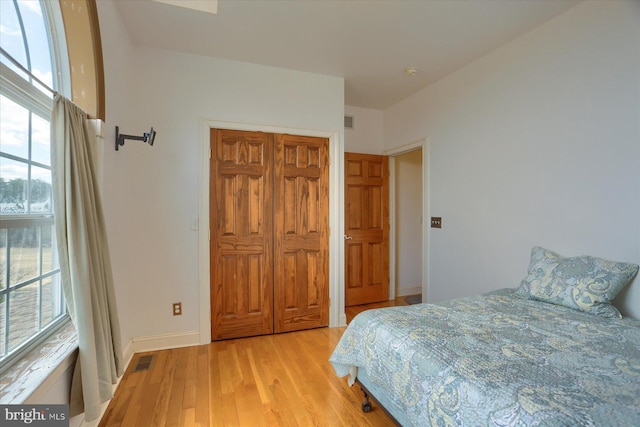 bedroom with light wood-type flooring, a closet, visible vents, and baseboards