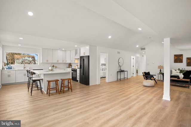 kitchen with lofted ceiling, a kitchen island, a breakfast bar, light countertops, and black appliances