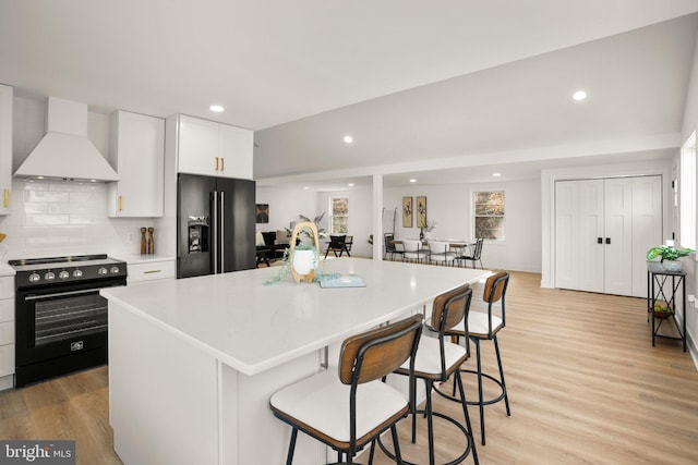 kitchen with range with electric cooktop, a center island, light wood-style floors, premium range hood, and black fridge