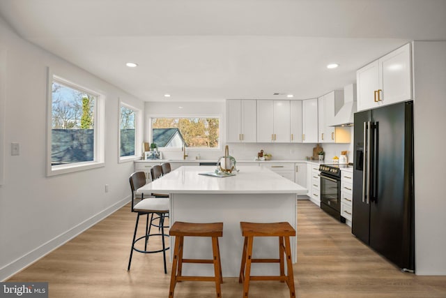 kitchen with custom exhaust hood, light countertops, light wood-style floors, black appliances, and a kitchen breakfast bar