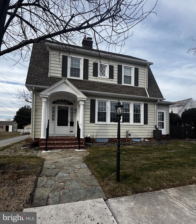 view of front of property with entry steps, roof with shingles, a front yard, and a chimney