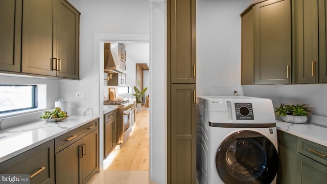 washroom with washer / clothes dryer, light wood-style flooring, and cabinet space