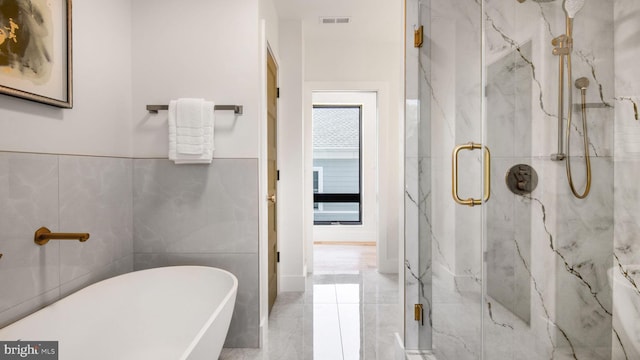bathroom with tile walls, a freestanding tub, a marble finish shower, and visible vents