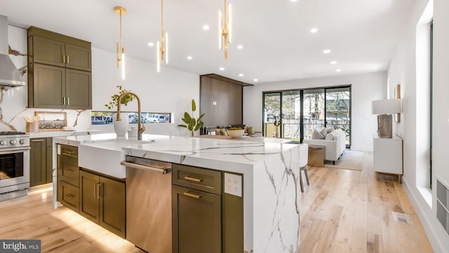 kitchen featuring stainless steel appliances, light wood-style flooring, a center island with sink, open floor plan, and light stone counters