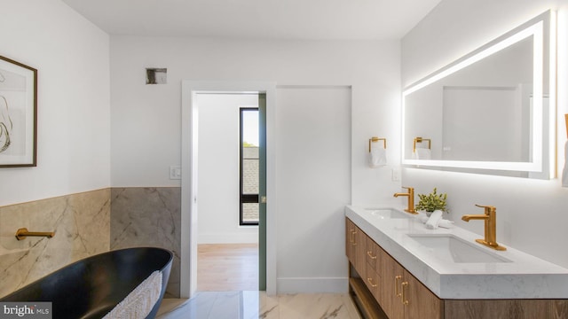 bathroom featuring marble finish floor, a freestanding tub, a sink, and double vanity
