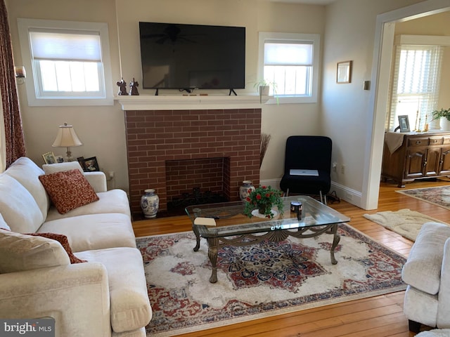 living room with a brick fireplace, baseboards, and hardwood / wood-style floors