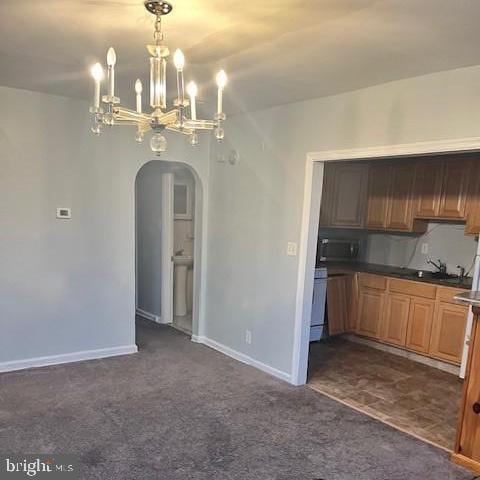 kitchen with arched walkways, pendant lighting, dark countertops, dark carpet, and brown cabinetry