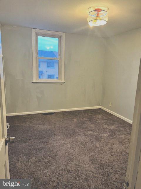 spare room featuring visible vents, dark carpet, and baseboards