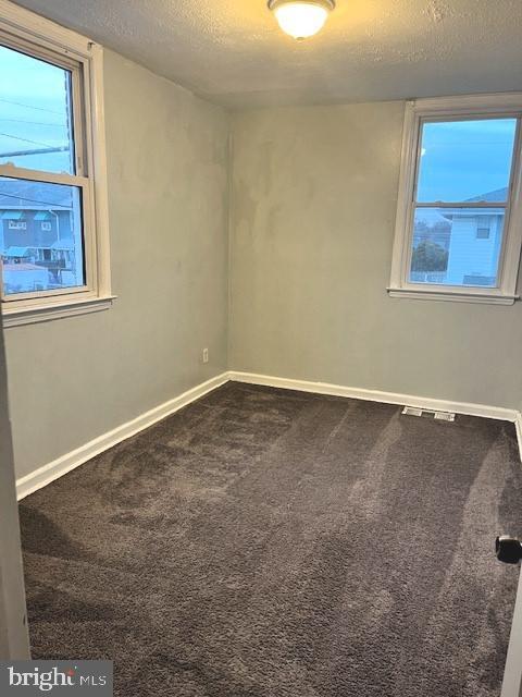 unfurnished room featuring a textured ceiling, carpet, and baseboards