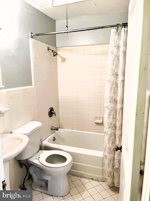 full bathroom featuring toilet, tile patterned flooring, shower / bath combination with curtain, and tile walls