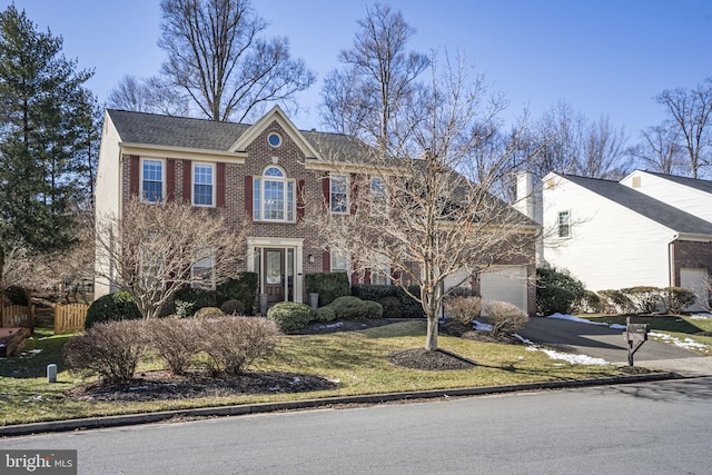 colonial-style house with driveway, a front yard, fence, and brick siding