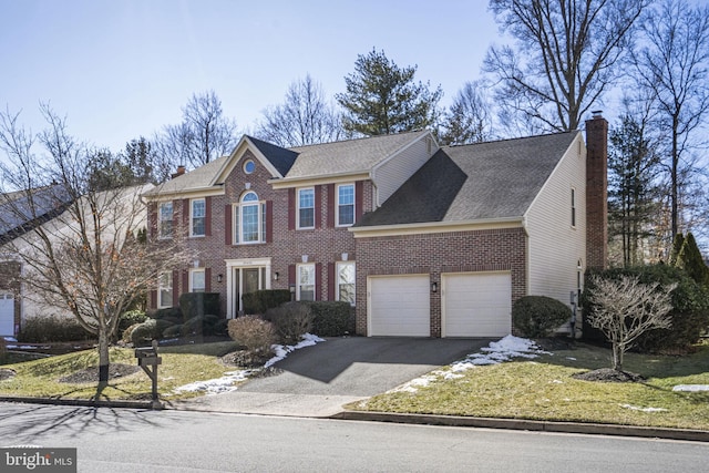 view of front of property featuring a garage, brick siding, driveway, a chimney, and a front yard