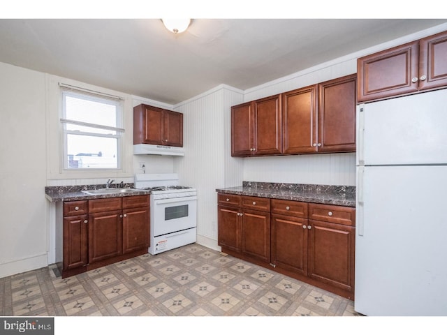 kitchen featuring white appliances, dark stone countertops, light floors, under cabinet range hood, and a sink