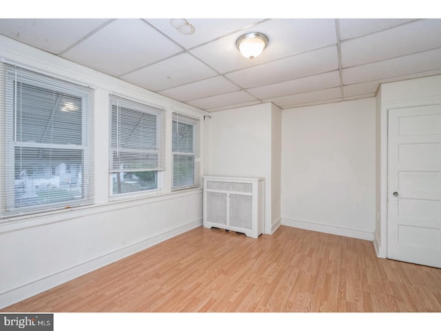 spare room featuring a paneled ceiling, radiator, baseboards, and wood finished floors