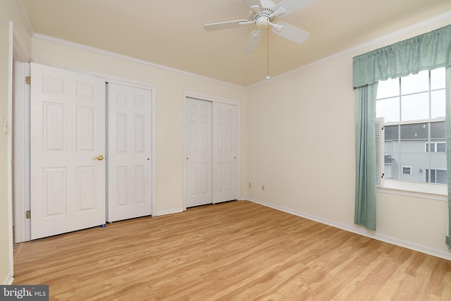 unfurnished bedroom featuring light wood-type flooring, two closets, crown molding, and baseboards