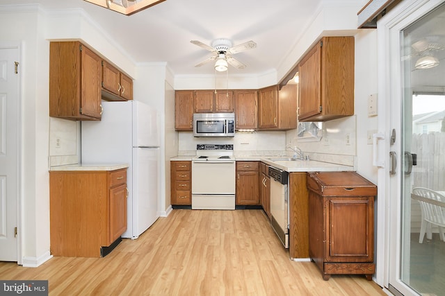 kitchen featuring a sink, white appliances, brown cabinetry, and crown molding