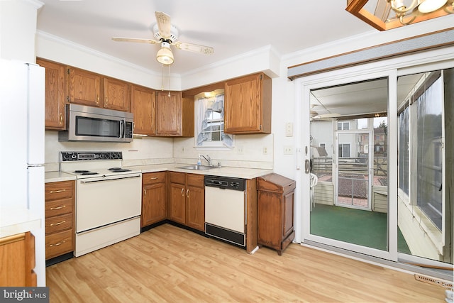 kitchen with a sink, white appliances, ornamental molding, and brown cabinetry