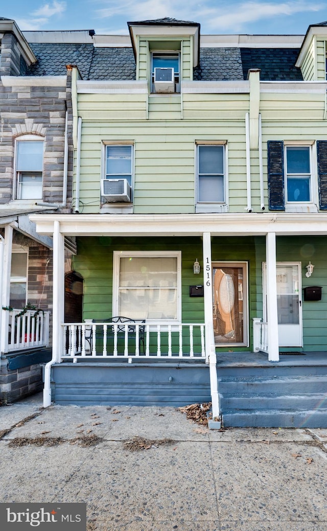 townhome / multi-family property with covered porch, mansard roof, and cooling unit