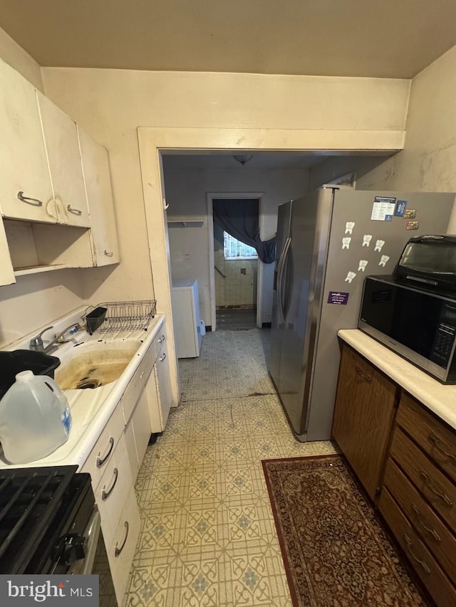 kitchen featuring washer / dryer, light countertops, light floors, white cabinetry, and a sink