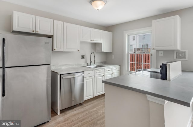 kitchen with light wood-style flooring, appliances with stainless steel finishes, a peninsula, white cabinetry, and a sink