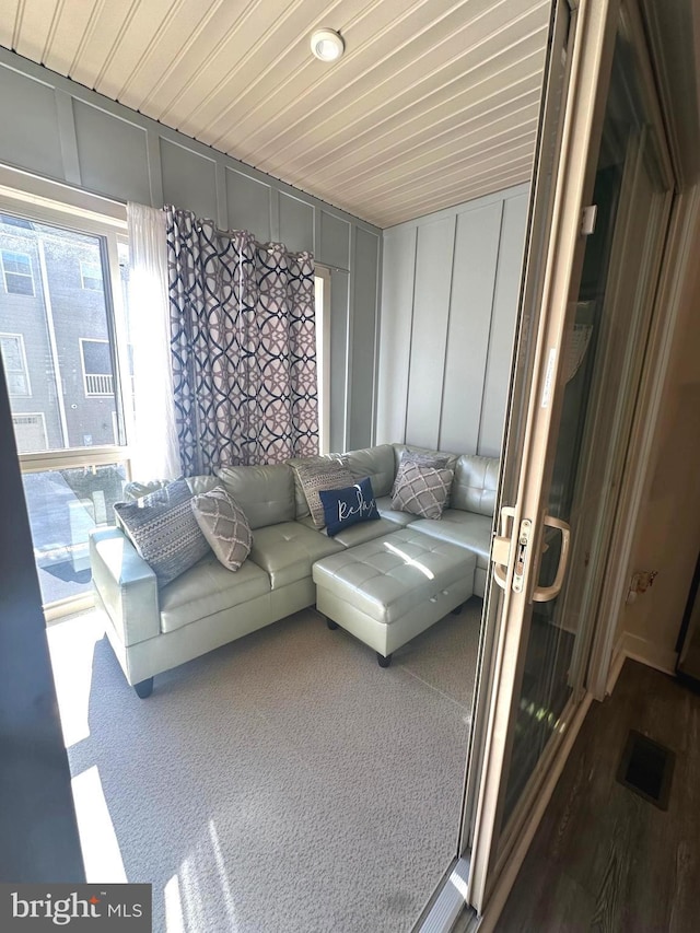 living room featuring carpet floors, wood ceiling, visible vents, and a decorative wall