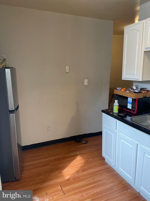 kitchen featuring dark countertops, light wood-style flooring, freestanding refrigerator, white cabinetry, and a sink