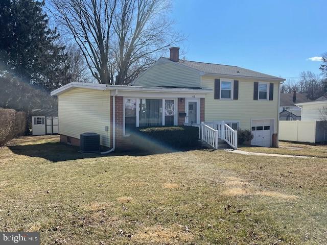 rear view of house featuring an attached garage, cooling unit, fence, a yard, and a chimney