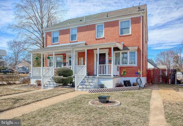 view of front of property featuring a front lawn, covered porch, brick siding, and a shingled roof