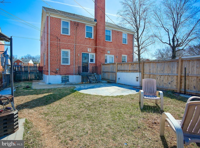 rear view of property with a yard, brick siding, a fenced backyard, and a chimney